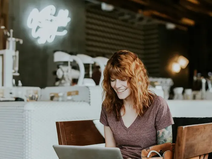 Smiling woman works on a laptop in a cafe, representing freelancers and small businesses listed on City Directory Central